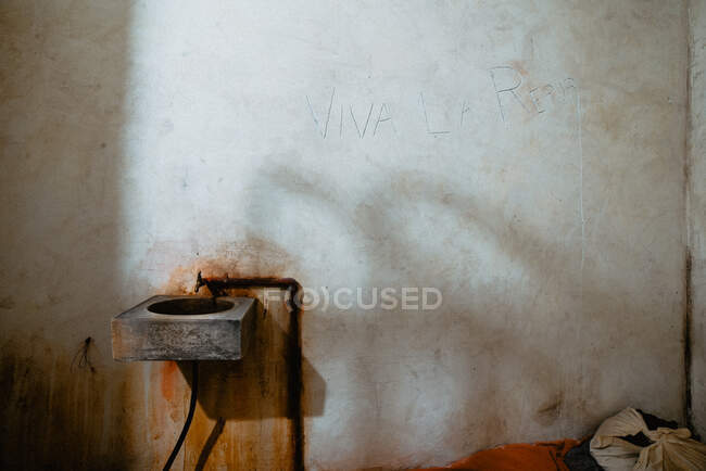 Грязная раковина, прикрепленная к обветшалой бетонной стене старой камеры тюрьмы в Овьедо, Испания — стоковое фото
