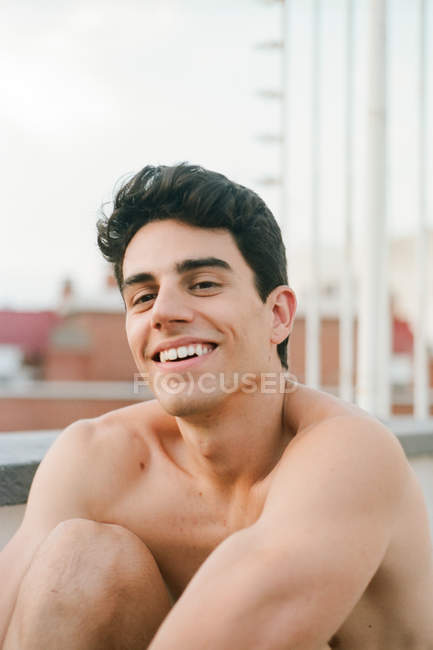 Brünett hemdloser junger Kerl schaut lächelnd in die Kamera — Stockfoto