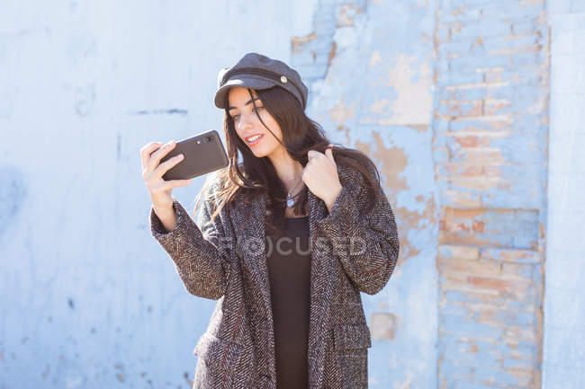 Affascinante signora ispanica scattare selfie con il telefono cellulare di fronte alla parete squallida — Foto stock