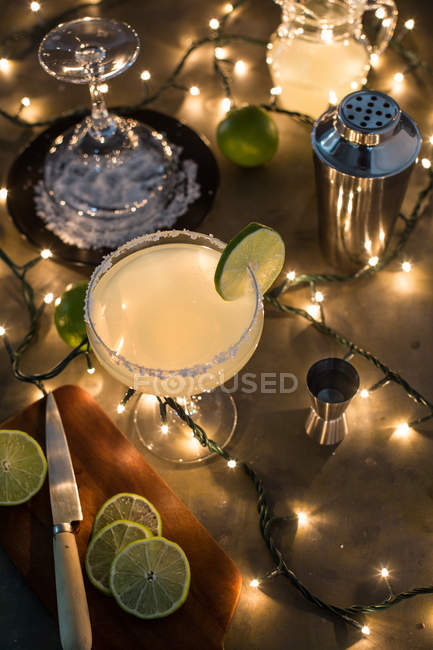 Margarita cocktail in glass on table with ingredients and lights — Stock Photo