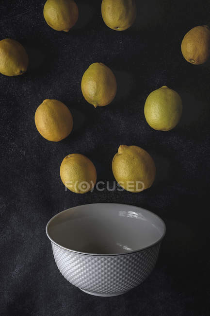 Свежие лимоны на темном фоне с белой миской — стоковое фото