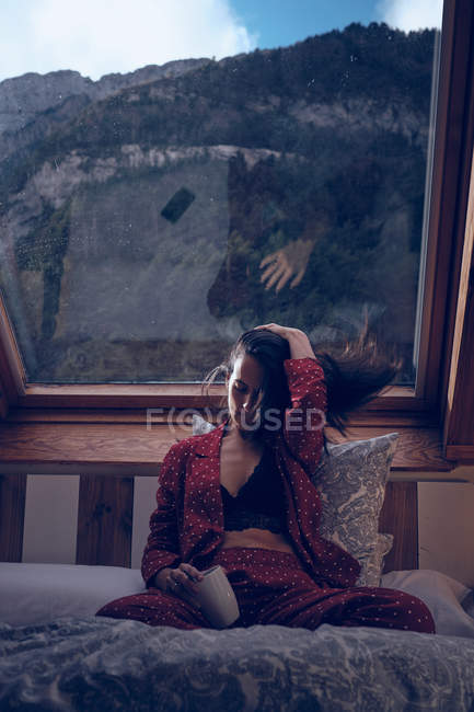Sensual female with mug sitting on bed — Stock Photo