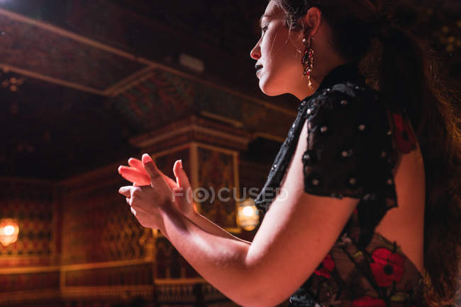 Vista laterale della giovane donna in abito battendo le mani e ballando sulla scena vicino a sedie in camera di lusso decorata da mosaico — Foto stock