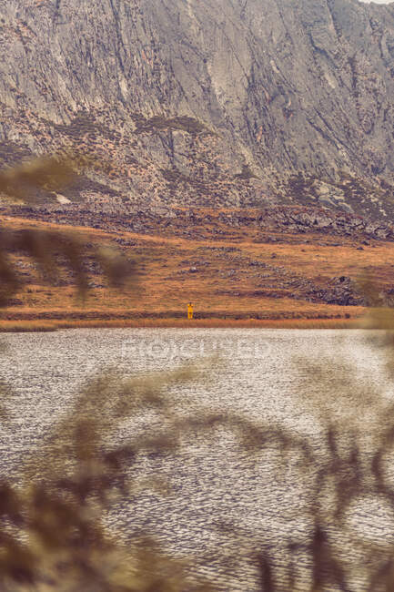 Persona in impermeabile giallo che va sulla riva del lago vicino a una montagna in Isoba, Castiglia e Leon, Spagna — Foto stock