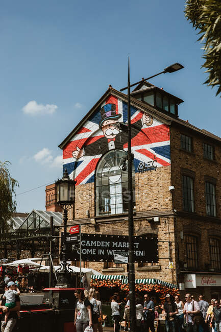 LONDON, VEREINIGTES KÖNIGREICH - 23. OKTOBER 2018: Menschenmassen spazieren in der Nähe eines alten Gebäudes mit einem erstaunlichen Gemälde auf dem Camden Lock Market an einem sonnigen Tag in London, England — Stockfoto
