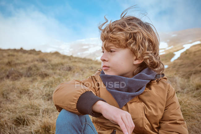 Милый мальчик, сидящий на холме возле ручья — стоковое фото