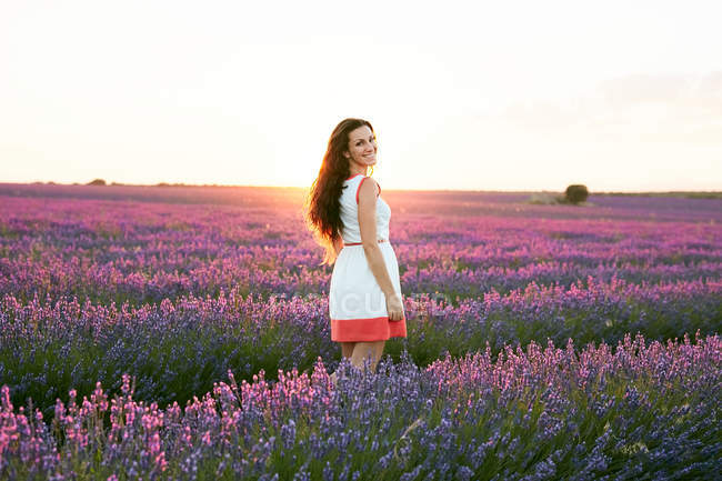 Frau steht bei Sonnenuntergang zwischen großen violetten Lavendelfeldern — Stockfoto