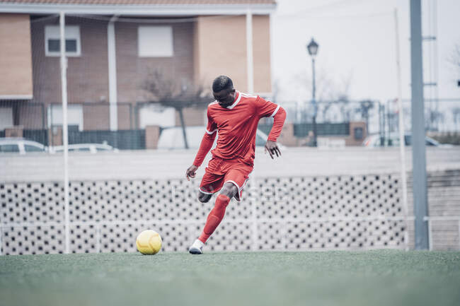 Afrikanischer Fußballer mit rotem Outfit beim Fußballspielen. — Stockfoto