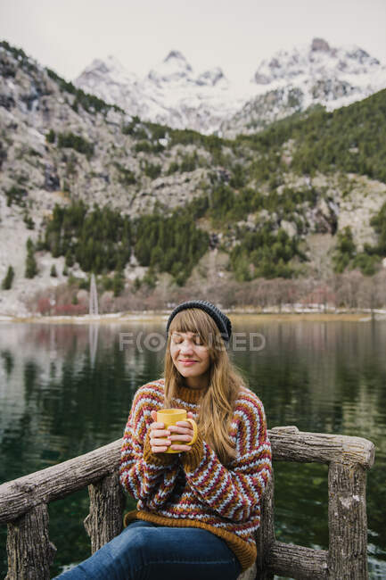 Young lady sitting on bench closed eyes near amazing view of water surface between high mountains with trees in snow in Pyrenees — Stock Photo