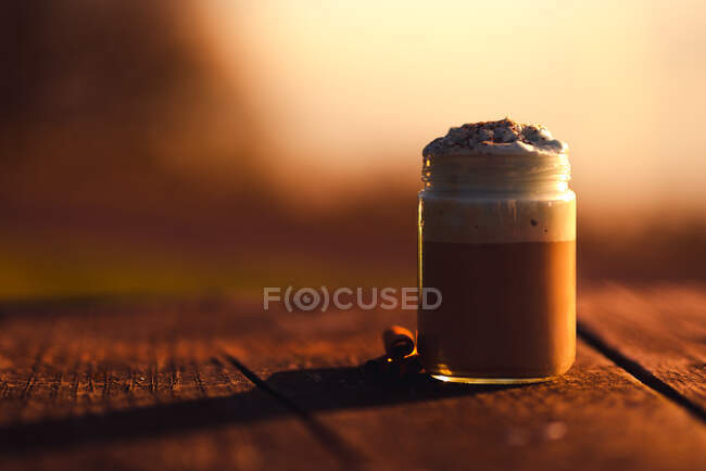Palitos aromáticos de canela cerca del frasco de delicioso café con crema en la mesa de madera - foto de stock