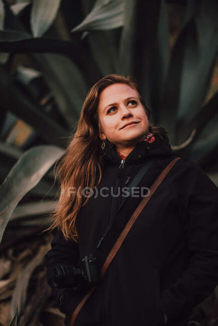 Frau im Mantel mit Kamera in der Nähe von Pflanzen — Stockfoto