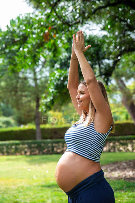 Усміхнена вагітна приваблива жінка тренується на килимку в парку — стокове фото
