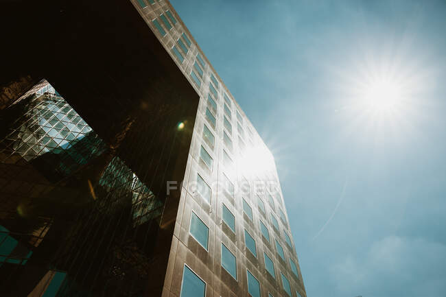 From below shot of bright sun shining on blue sky over facade of modern building on street of London, England — Stock Photo