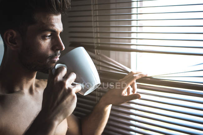 Пильний чоловік стоїть біля вікон, сліпих чашечкою кави. — стокове фото