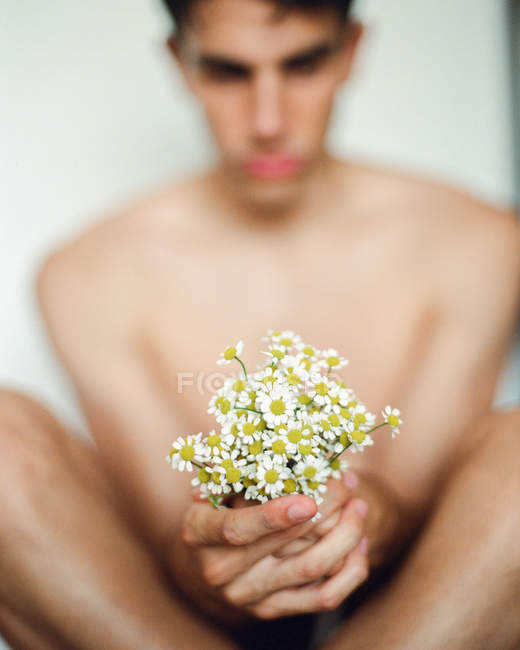Боковой вид молодого парня без рубашки со свежими белыми цветами в руках, смотрящего в сторону на размытом фоне — стоковое фото