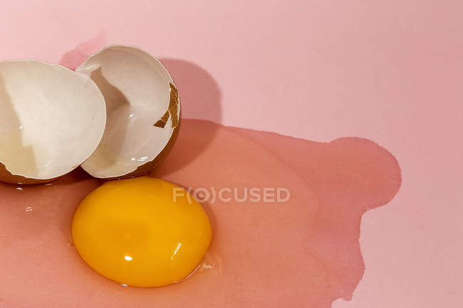 Yema de huevo cruda y cáscara de huevo sobre fondo rosa - foto de stock