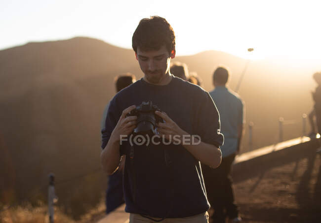 Young guy looking at camera?in hands near people on mountain at sunset in San Francisco, USA — Stock Photo