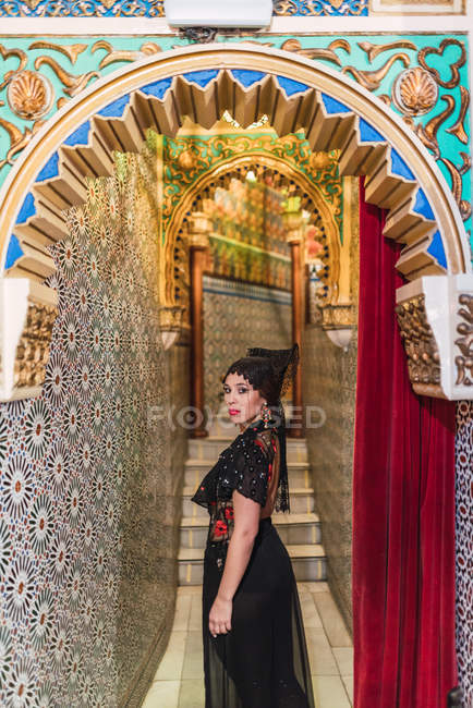 Vista laterale di appassionata giovane donna in abito in piedi in stretto corridoio decorato da mosaico — Foto stock