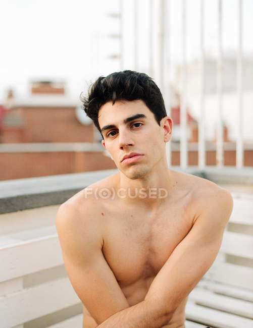 Giovane ragazzo senza maglietta guardando la fotocamera e seduto sul balcone su sfondo sfocato — Foto stock