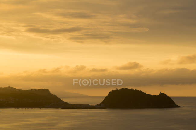 View of cliffs in peaceful water of sea illuminated with golden sunset light — Stock Photo