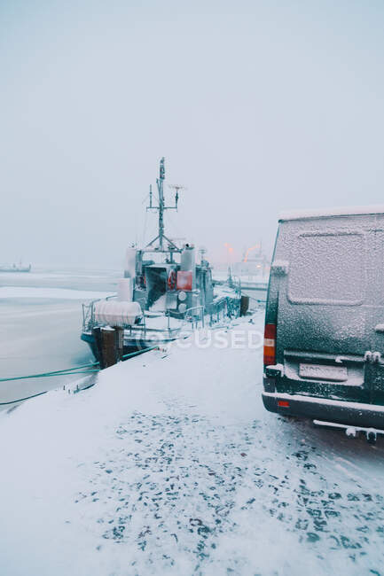 Furgoneta moderna y pequeño barco de pie en el puerto de la ciudad ártica nevada en día gris - foto de stock