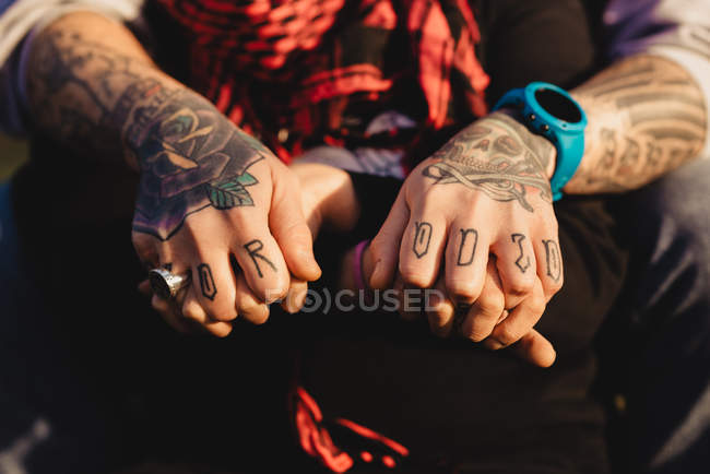 Cropped image of man in tattoos with ring and watch holding hands of woman with red scarf in sunny weather — Stock Photo