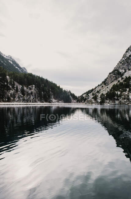 Дивовижний вид поверхні води між високими горами з деревами в снігу і хмарному небі в Піренеях. — стокове фото