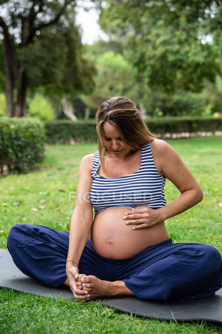 Donna attraente incinta che medita sul tappeto nel parco — Foto stock