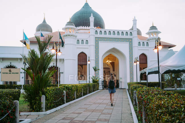 Back view young slim lady with backpack walking on walkway near big white cathedral in Malaysia — Stock Photo
