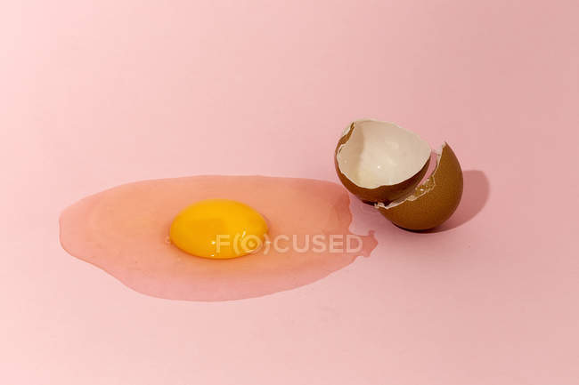Raw egg yolk and eggshell on pink background — Stock Photo