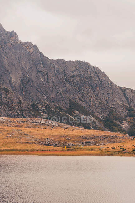 Person in yellow raincoat going on shore of lake near a mountain in Isoba, Castile and Leon, Spain — Stock Photo
