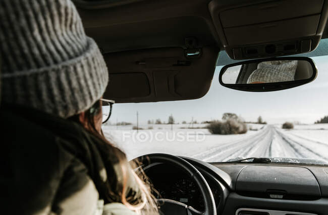 Vue arrière de dame au chapeau conduite automobile sur route de campagne dans la neige entre champ à Vilnius, Lituanie — Photo de stock