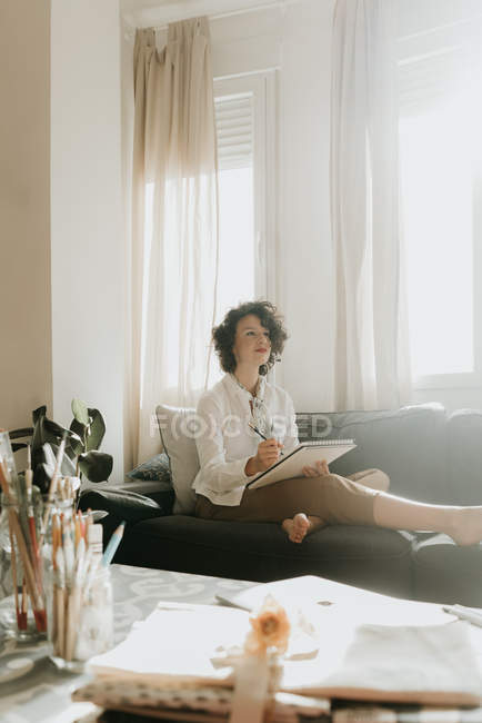 Жінка пише на папері на дивані в кімнаті — стокове фото