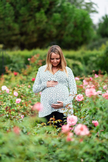 Sonriendo embarazada atractiva mujer entre flores - foto de stock