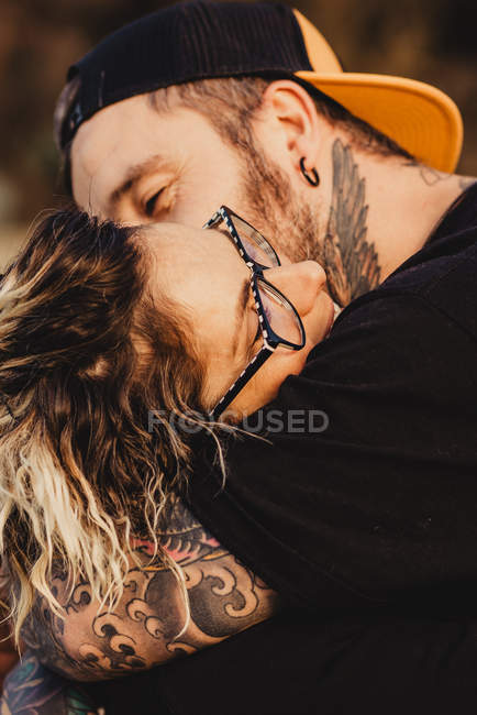 Hombre barbudo abrazando mujer alegre cerca de la madera en el bosque sobre fondo borroso - foto de stock