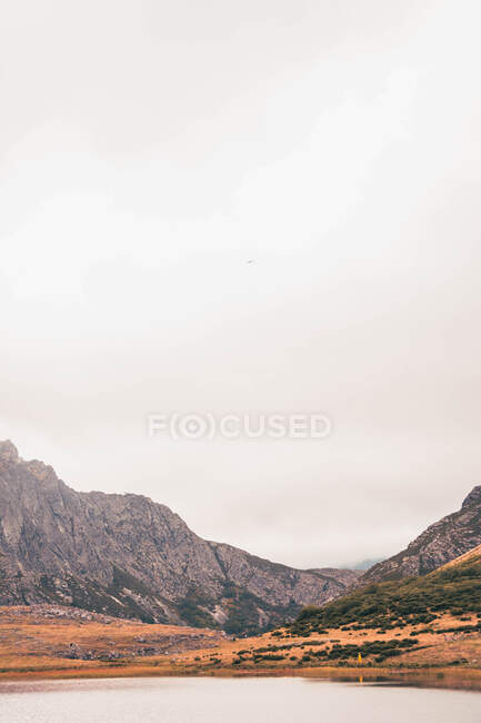 Persona en impermeable amarillo que va a la orilla del lago cerca de Wigwam y colina en Isoba, Castilla y León, España - foto de stock