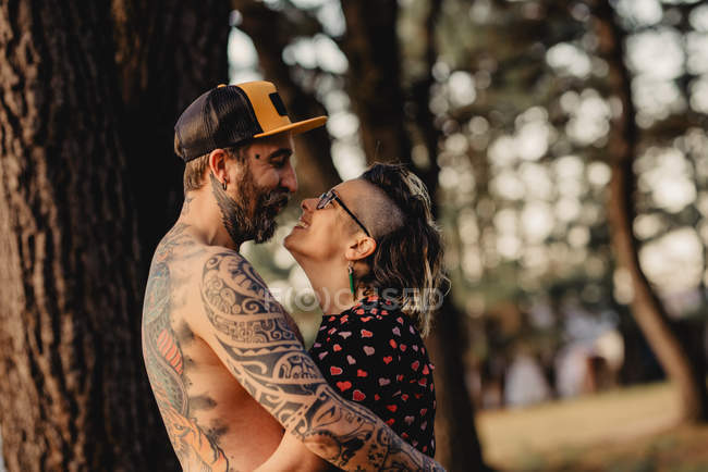 Homme barbu embrassant femme gaie près du bois dans la forêt sur fond flou — Photo de stock