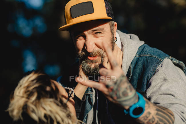 Bearded man embracing woman near wood in forest and showing rock sign — Stock Photo