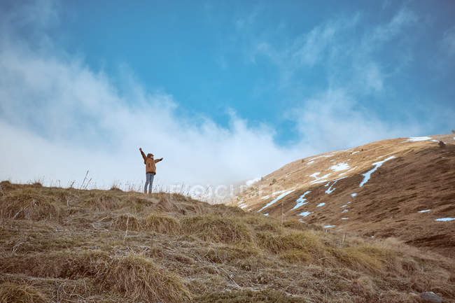 Unrecognizable kid in warm clothes standing on top of hill against cloudy sky in autumn countryside — Stock Photo