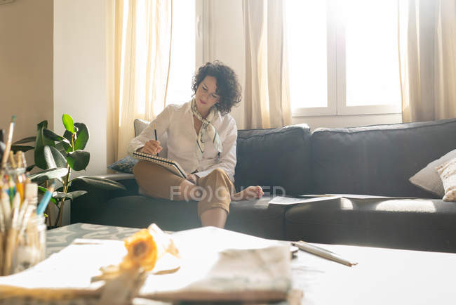 Frau schreibt auf Papier auf Sofa im Zimmer — Stockfoto