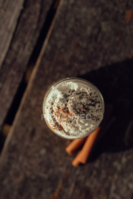 Aromatic cinnamon sticks near jar of yummy coffee with cream on lumber tabletop — Stock Photo