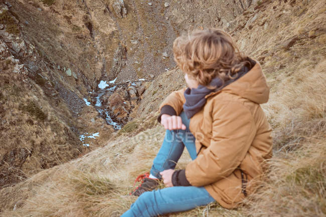 Carino ragazzo seduto sulla collina vicino al ruscello — Foto stock