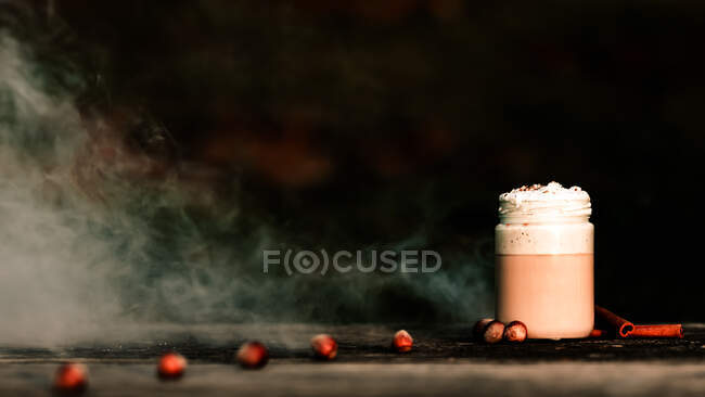 Dünner weißer Qualm breitet sich über der Tischplatte mit einem Glas mit frischem Kaffee und aromatischen Gewürzen aus — Stockfoto