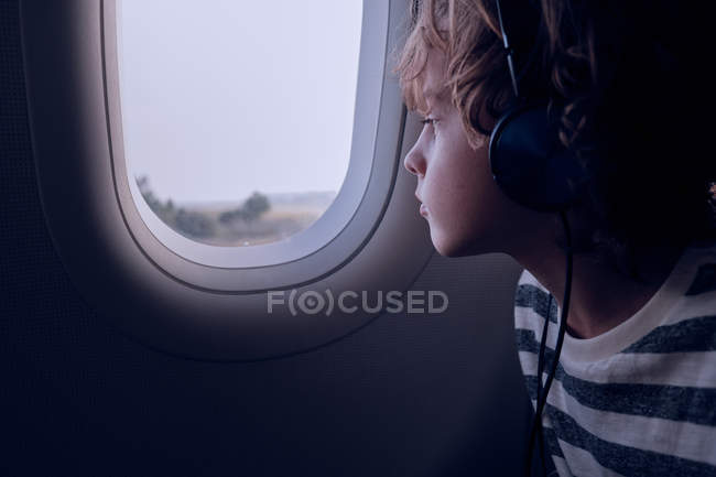 Garçon mignon avec écouteurs dans l'avion — Photo de stock
