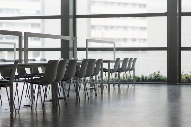 Современные столы и удобные стулья, стоящие возле огромных окон в просторном офисе — стоковое фото