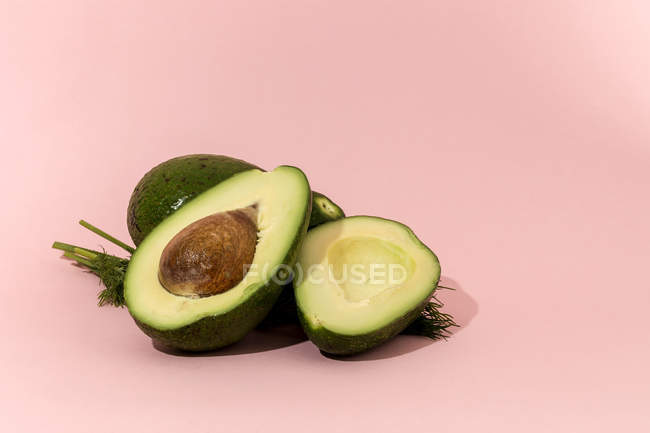 Fresh whole and halved avocados on pink background — Stock Photo