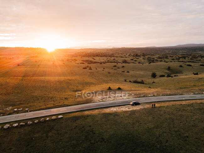 Величественный вид беспилотника яркое солнце садится на облачном вечернем небе над удивительным полем и асфальтовой сельской дороге в Наварре, Испания — стоковое фото