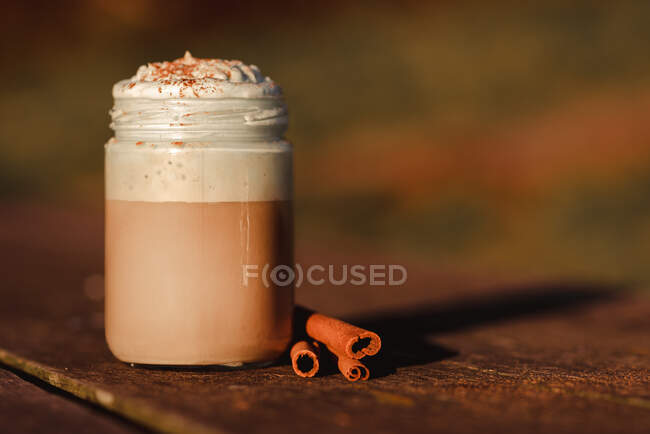 Cannella aromatica bastoncini vicino barattolo di caffè gustoso con crema su legno da tavolo — Foto stock