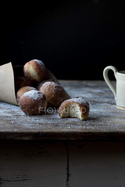 Fresh cake near set of baked loaf in craft paper with powdered sugar on wooden table in darkness on black background — Stock Photo