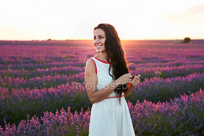 Жінка стоїть між великим фіолетовим лавандовим полем на заході сонця — стокове фото